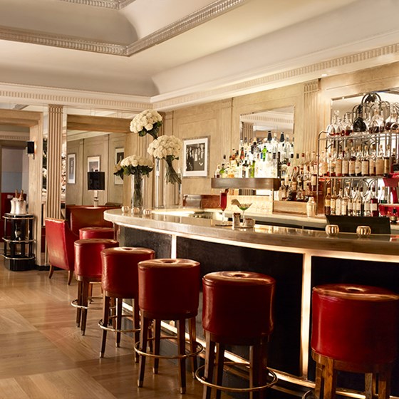 Claridge's Bar. An image of Claridge's Bar with red bar stools lined up against the bar. Behind the bar are well stocked shelves of alcohol.