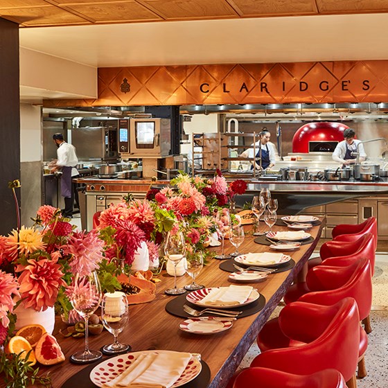 L'Epicerie at Claridge's, a beautiful table set up with tableware and flowers, and the open kitchen  behind it