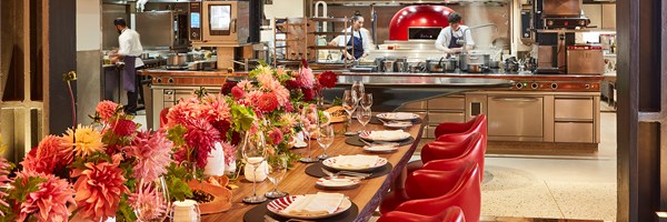 L'Epicerie at Claridge's, a beautiful table set up with tableware and flowers, and the open kitchen  behind it.