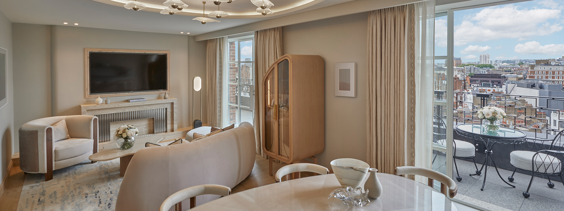 Claridge's Terrace Suite - lounge with dining table, couches, TV on the wall and a terrace with chairs.