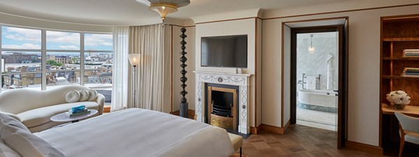 The Mews Pavilion at Claridge's - bedroom view with bed, fireplace, terrace with rooftop view, and  bathroom on the background on the right hand side of the image.