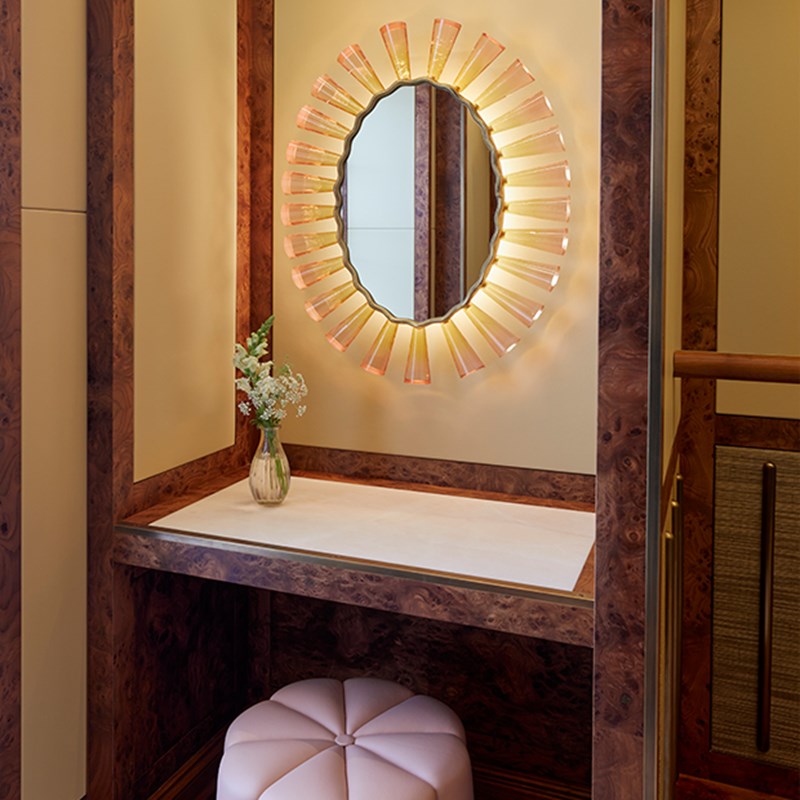 The Mews Pavilion at Claridge's - makeup area in the dressing room with mirror on the wall, flowers on the table and cushioned seat.