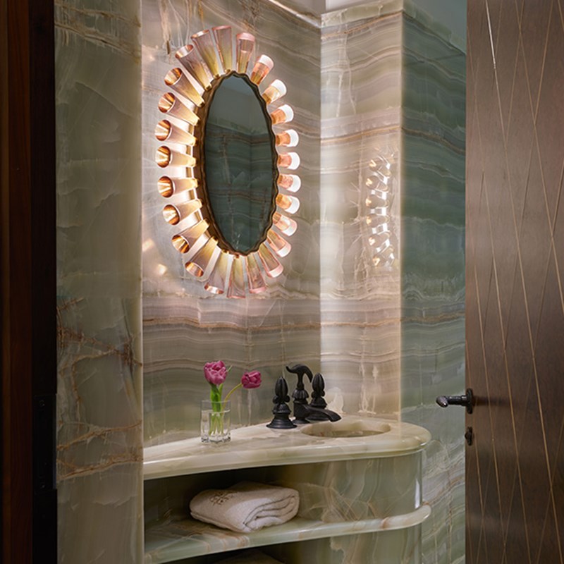 Marble bathrub with a mirror above it and a flower in a vase next to it.