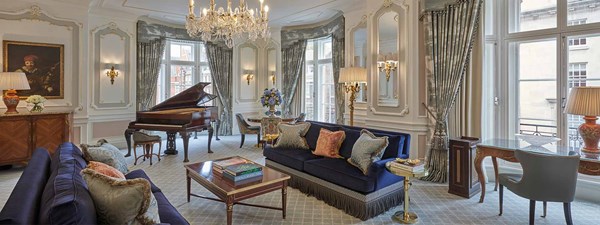 Prince Alexander Suite at Claridge's - lounge area with blue couches and wooden coffee table in the middle, grand piano in the back and dining table in the corner.