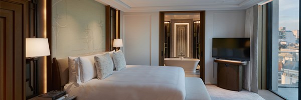 Master bedroom with white bedding on large bed facing the floor to ceiling windows